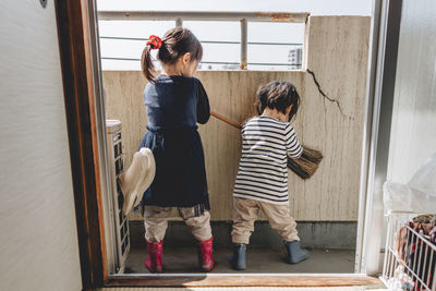 Sisters cleaning the wall of balcony with broom stick