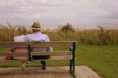 Empty bench on field against cloudy sky