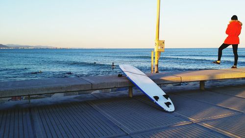 Person standing by surfboard against sea