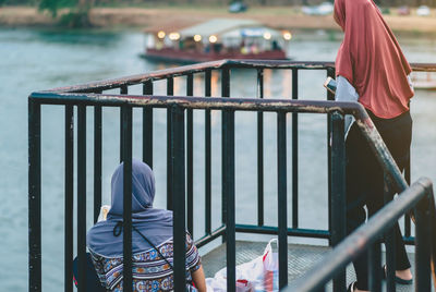 Rear view of people standing by railing against river