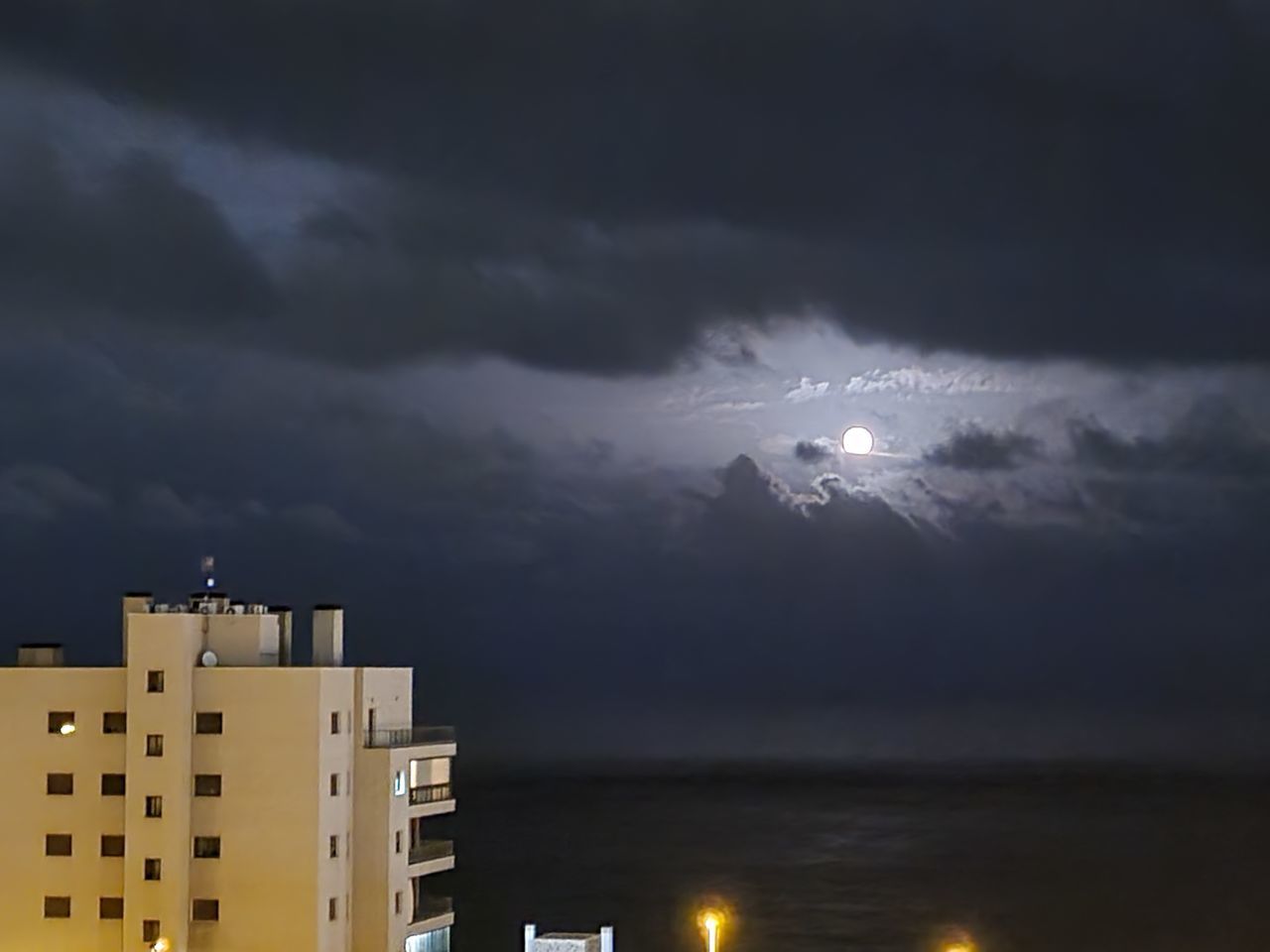 sky, cloud, storm, architecture, building exterior, night, building, built structure, city, thunderstorm, storm cloud, illuminated, lightning, nature, horizon, thunder, power in nature, dramatic sky, no people, dusk, residential district, environment, evening, moon, cityscape, water, outdoors, beauty in nature, dark, overcast, light, darkness, office building exterior, city life, rain, full moon, apartment