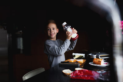 Happy boy showing jam bottle while standing at kitchen counter