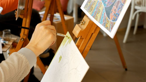 Cropped hand of artist painting easel art on canvas at studio