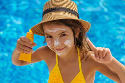Portrait of smiling girl applying suntan lotion in swimming pool