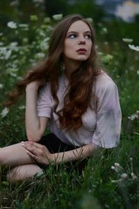 Young woman looking away while sitting on grassy land