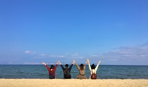 Rear view of friends with arms raised at beach against sky