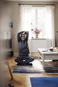 Senior man stretching arms while doing yoga in living room at home