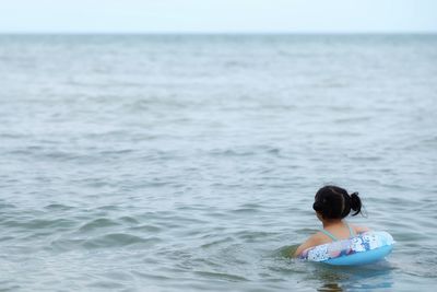 Rear view of girl with inflatable ring swimming in sea