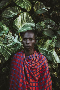 Maasai man in traditional clothes standing in front of green leaves