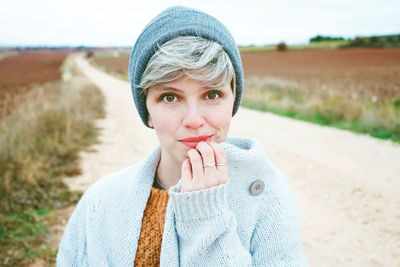 Close-up portrait of woman wearing knit hat while standing on dirt road