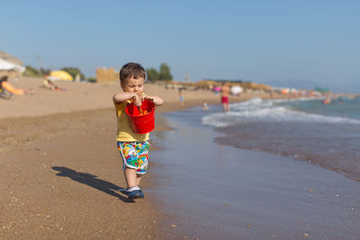 Full length of boy holding bucket on shore at beach