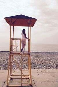 Rear view of woman standing on lifeguard hut at beach