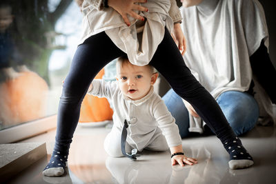 Smiling baby crawling on the floor between his sister's legs