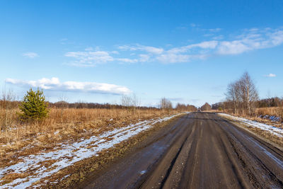 Road leading towards snow covered landscape against blue sky