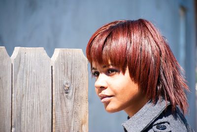 Close-up of woman looking away while standing by wooden fence