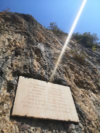 Low angle view of text on rock against sky