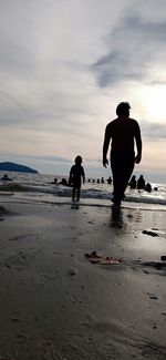 Rear view of silhouette men on beach against sky during sunset