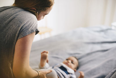 Mother talking through mobile phone while dressing toddler on bed at home