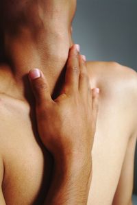 Midsection of shirtless man touching neck with hand against gray background