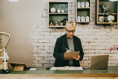 Senior female owner preparing checklist while working at interior shop