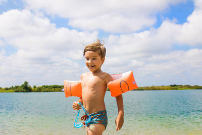 Boy wearing water wings by sea against sky