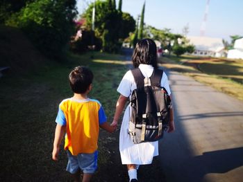 Rear view of siblings walking on road