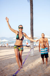 Woman slacklining at beach against sky