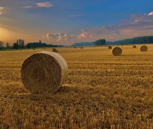 Hay bales on field against sky during sunset