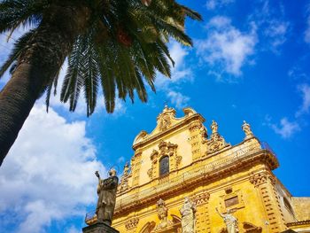 Low angle view of historic church by palm tree against sky