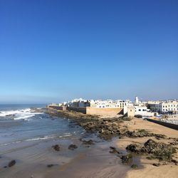 Scenic view of beach and buildings against clear blue sky