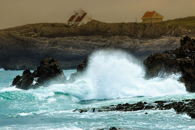 Waves splashing on rocks at shore against sky