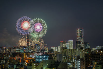 Firework display in city against sky at night