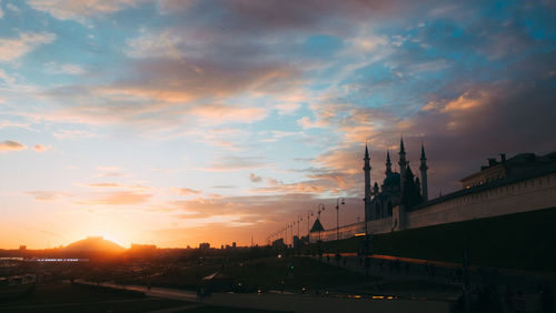 Road by buildings against sky during sunset