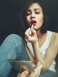 Young woman applying lipstick against black background