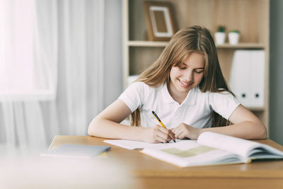 A smiling girl does her homework, writes a synopsis, and prepares for lectures. 