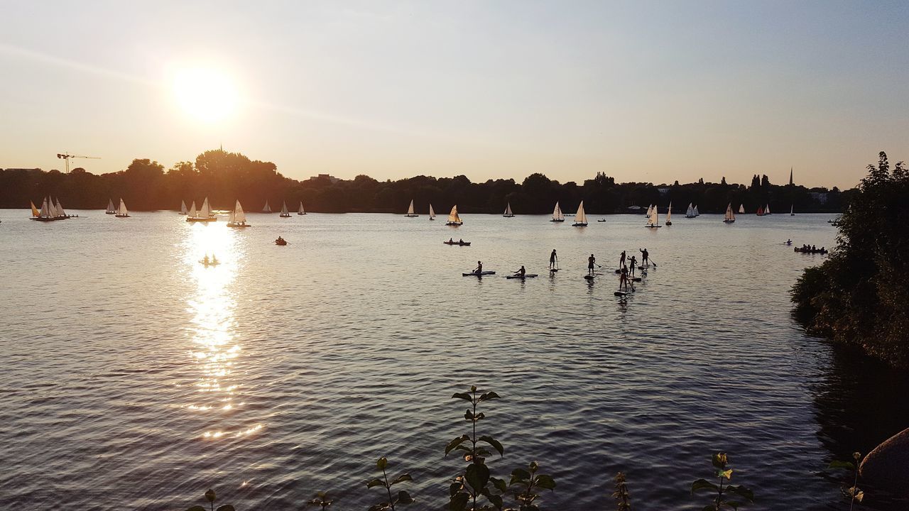 SILHOUETTE PEOPLE SWIMMING IN LAKE AGAINST SUNSET SKY