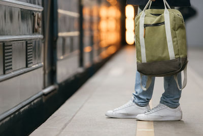 Male waiting subway train on platform. handsome man in white sneakers and jeans with green backpack