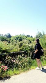 Full length of young woman walking on grass against clear sky