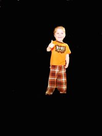 Portrait of smiling boy standing against black background