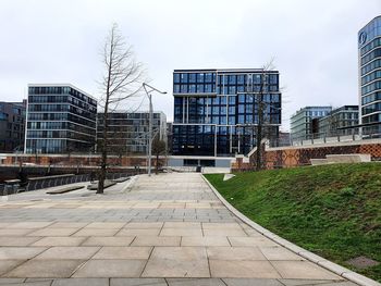 Footpath by buildings in city against sky