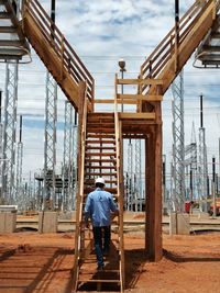 Rear view of man working on ladder against sky