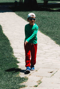 Full length of boy walking on footpath at park on sunny day