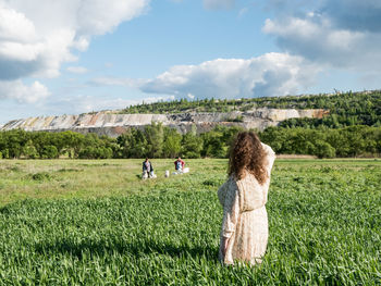 Rear view of women sitting on field against sky