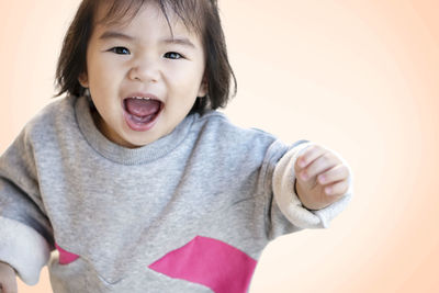 High angle portrait of cute baby girl with mouth open standing against beige background