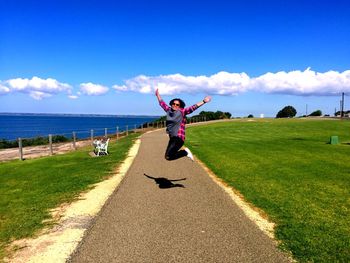 Full length of man jumping over sea against blue sky