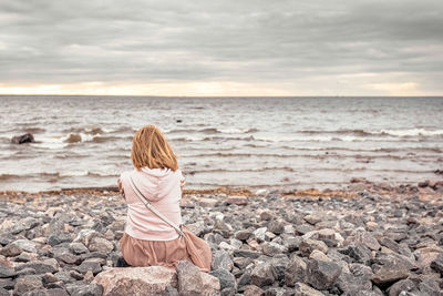 Rear view of woman on rock at beach against sky