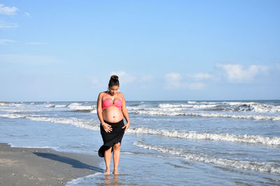 Rear view of young woman standing at beach against sky