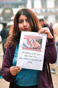 Portrait of smiling young woman holding paper with text