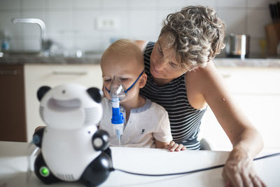 Boy at home inhaling while sitting at mothers lap