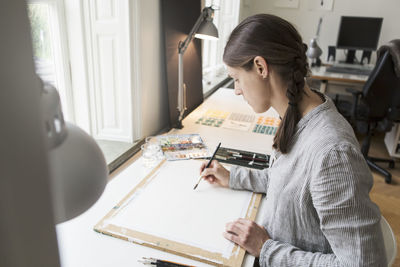 High angle view of artist painting on canvas at table in creative office